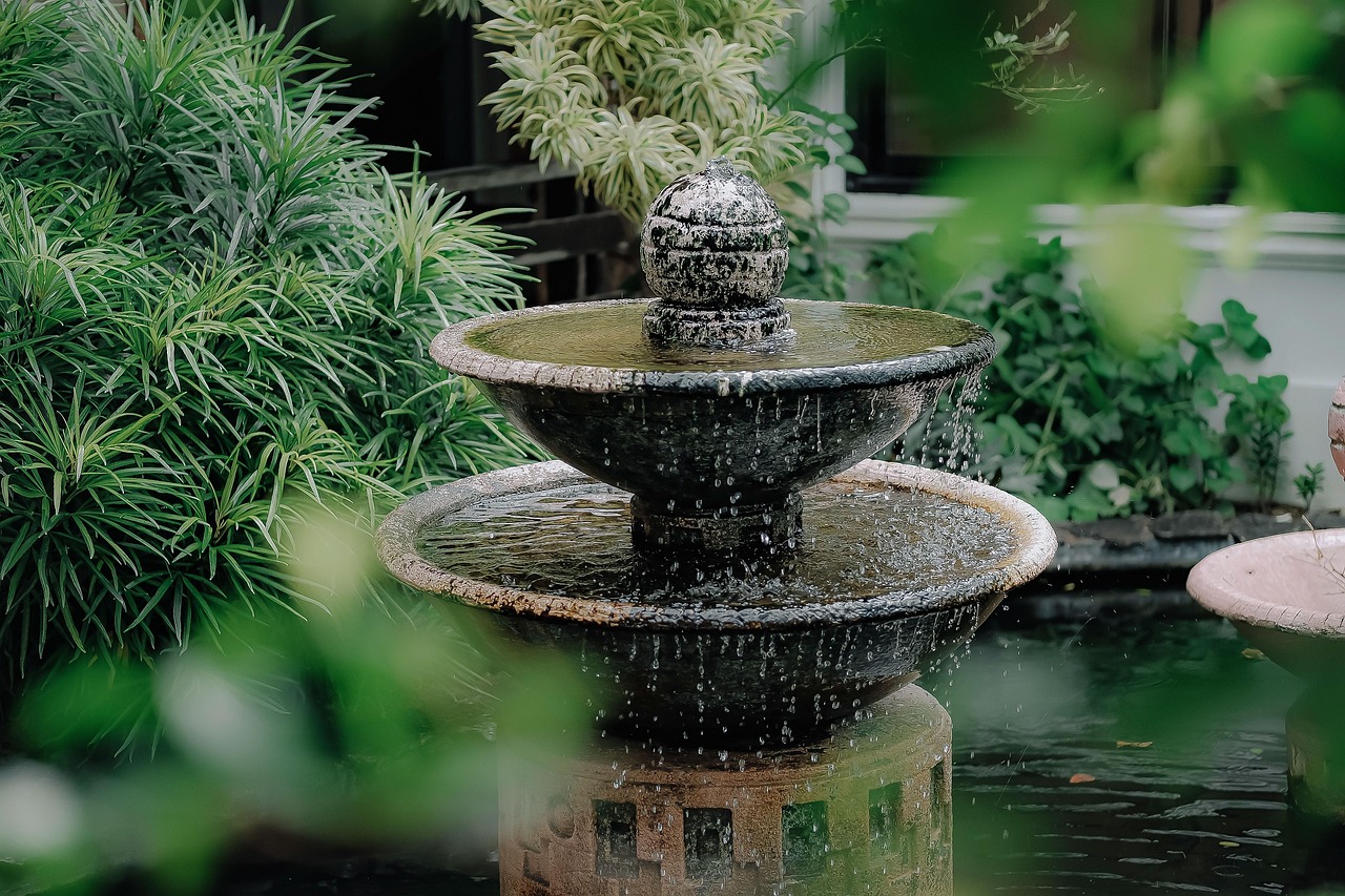 Gartenbrunnen mit zwei Schalen und Wasserspiel, umgeben von Grünpflanzen.