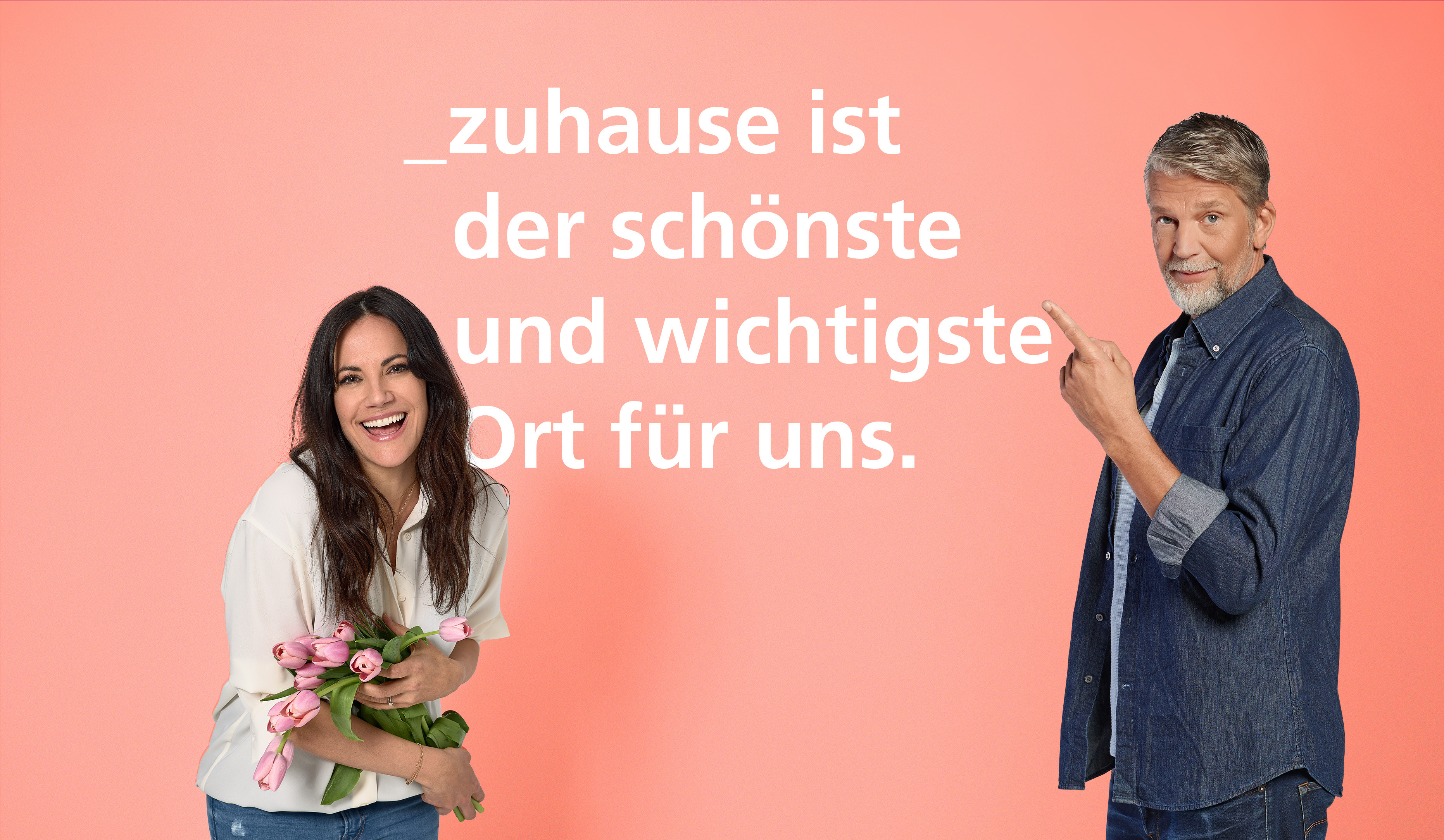 Eine Frau auf der linken Seite und ein Mann auf der rechten Seite, die Frau hält rosten Tulpen in der Hand und lacht in die Kamera, der Mann zeigt, während er in die Kamera schaut, auf den Text, der sagt "Zuhause ist der schönste und wichtigste Ort für uns"