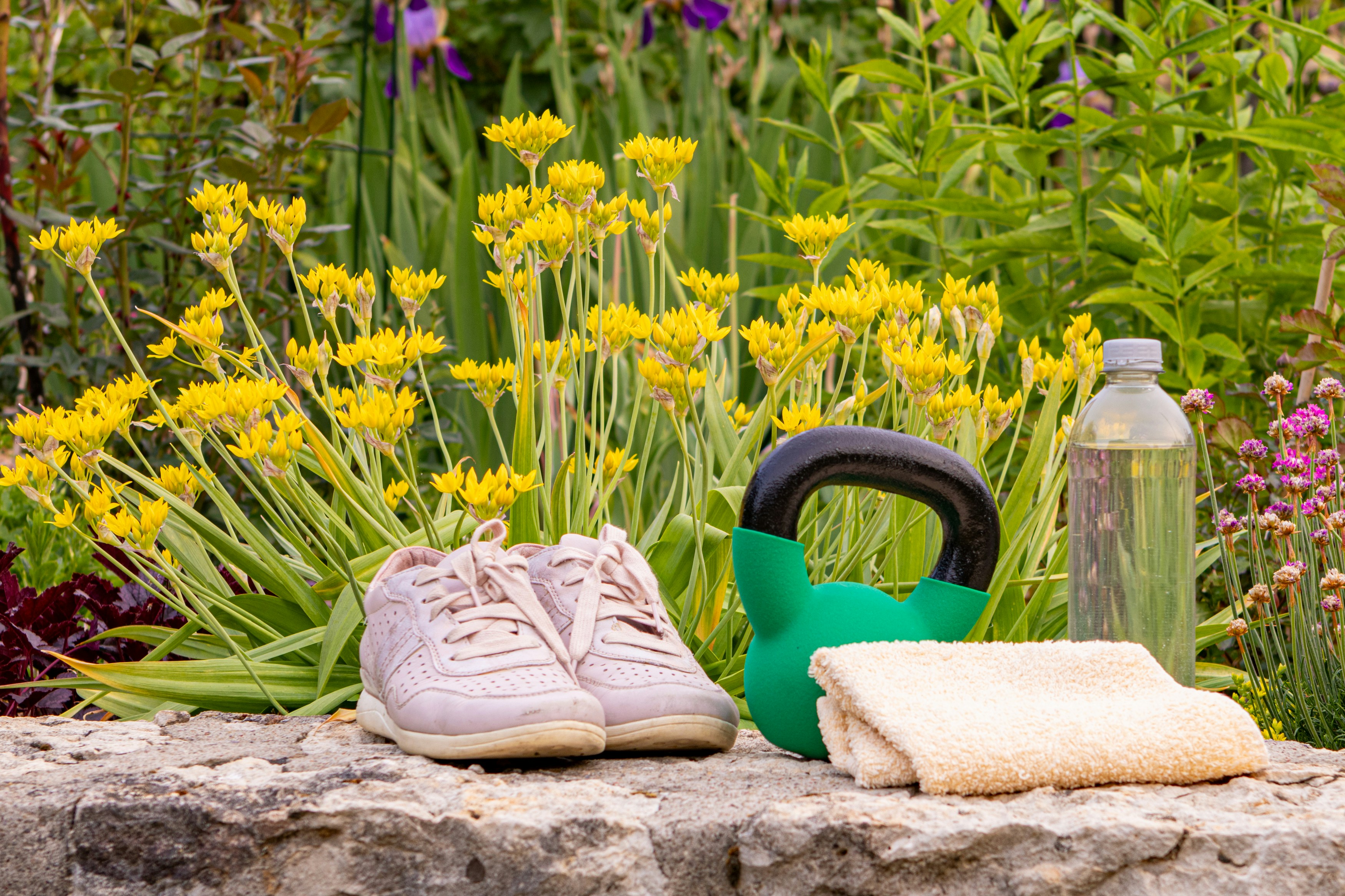 Rosa Turnschuhe, Kettlebell, Wasserflasche und Handtuch auf Stein; Sommerfitness im Freien.