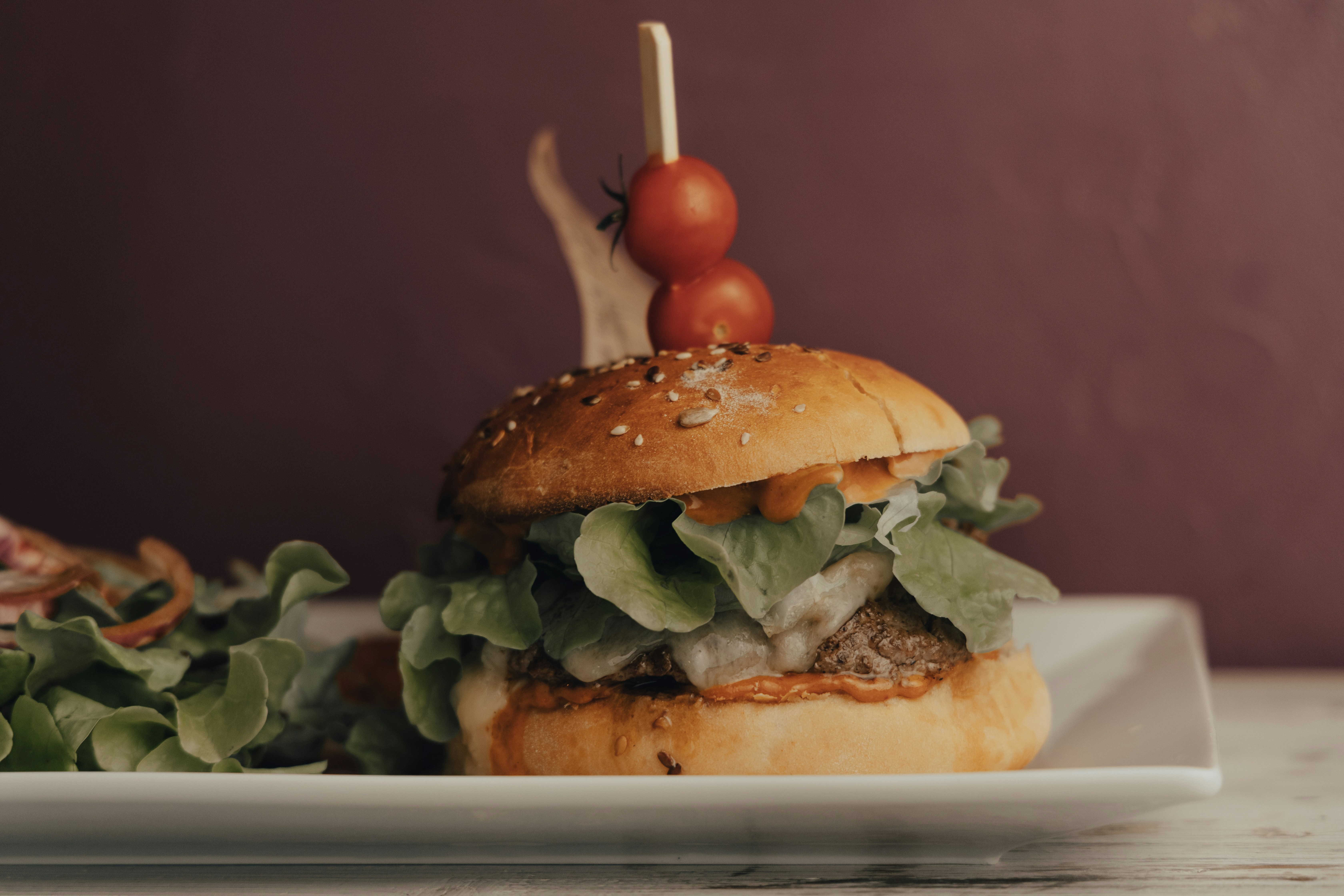 Nahaufnahme eines köstlichen veganen Burgers mit Salat, Tomaten und einem Sesambrötchen. Perfekt für Sommergrillabende und Picknicks!