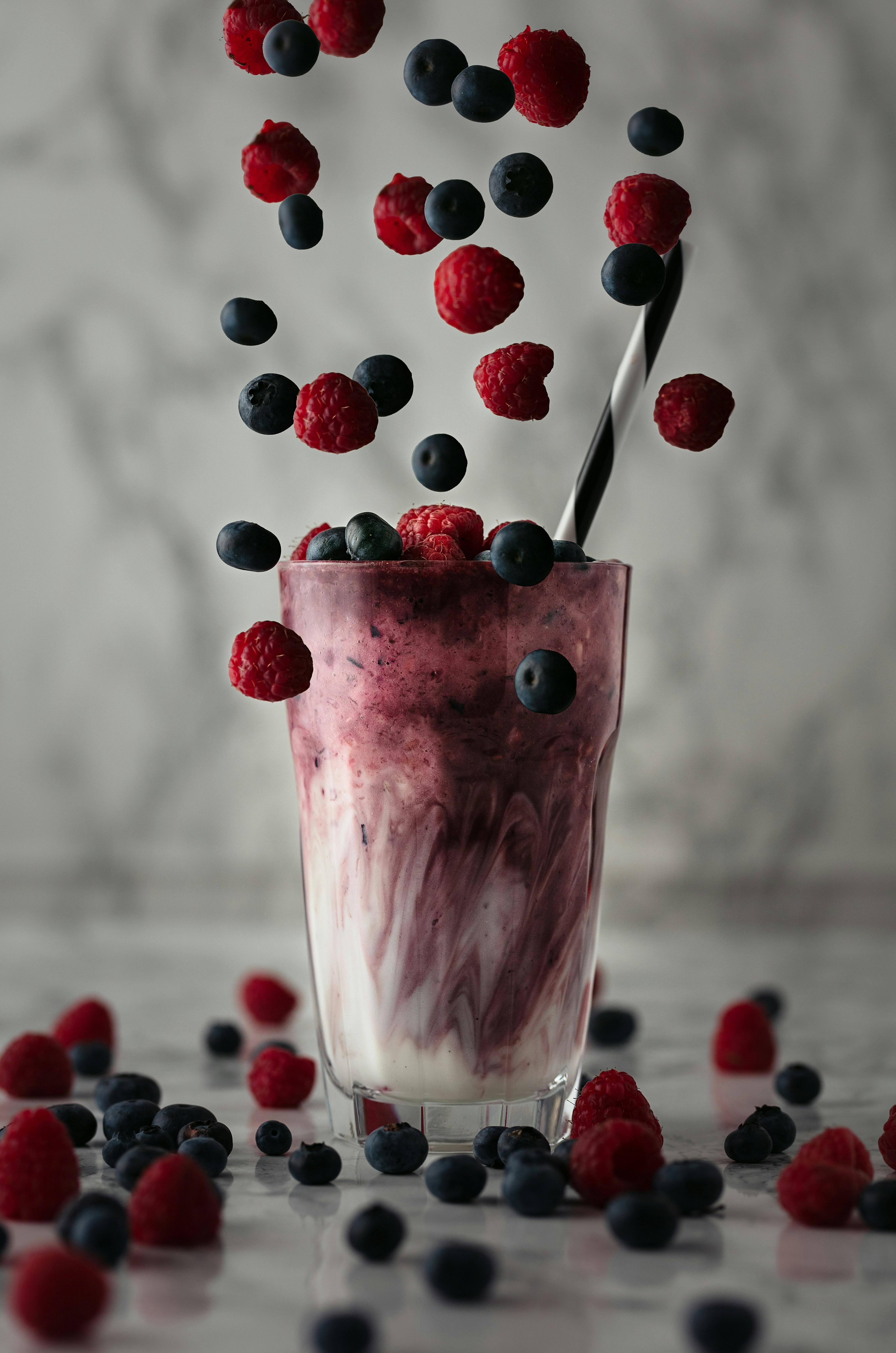 Erfrischender Beeren-Smoothie mit Himbeeren und Blaubeeren, die ins Glas fallen. Perfektes Sommergetränk.