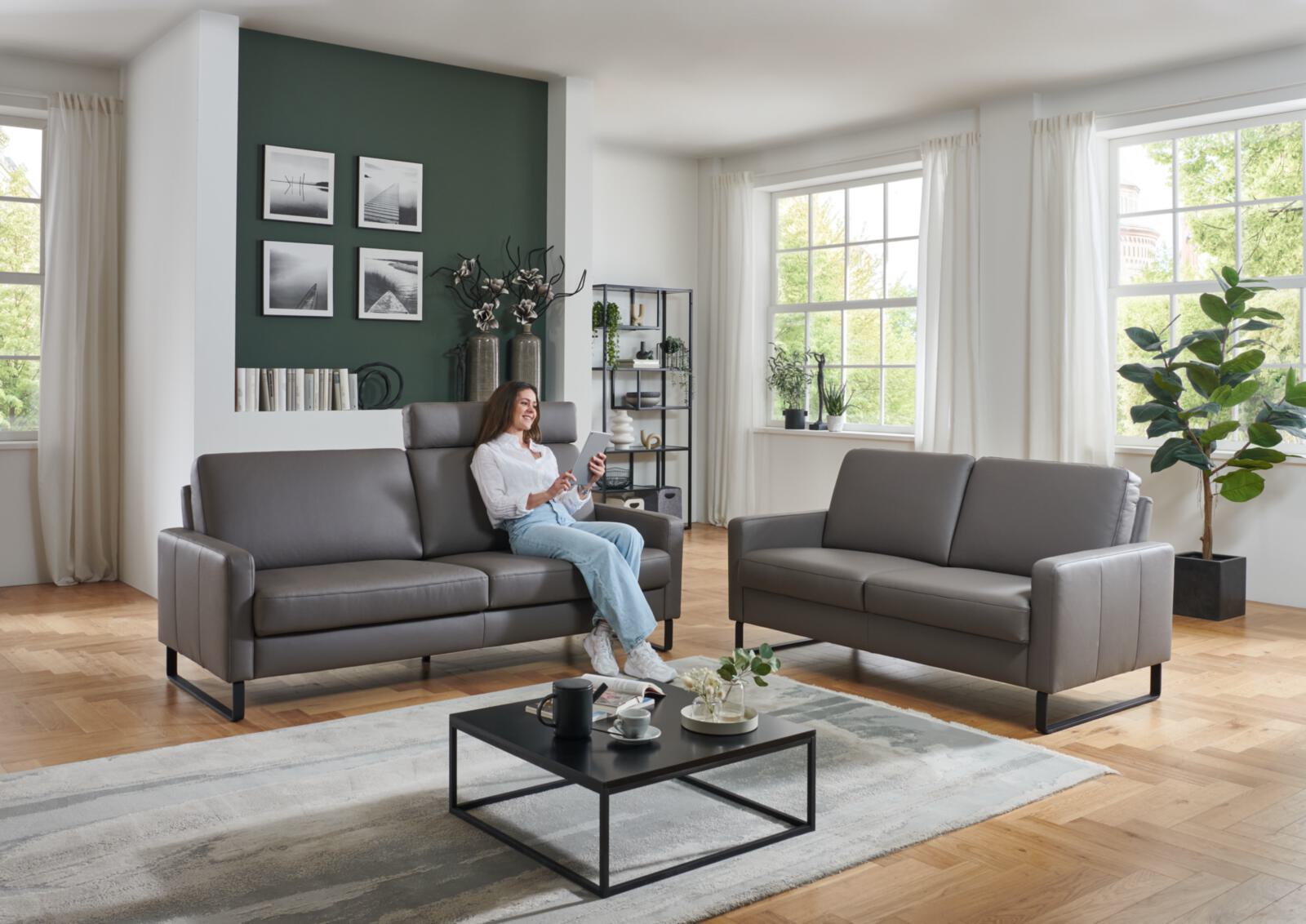 Modernes Wohnzimmer mit grauer Couchgarnitur, Frau mit Tablet auf Sofa, Couchtisch und Teppich.