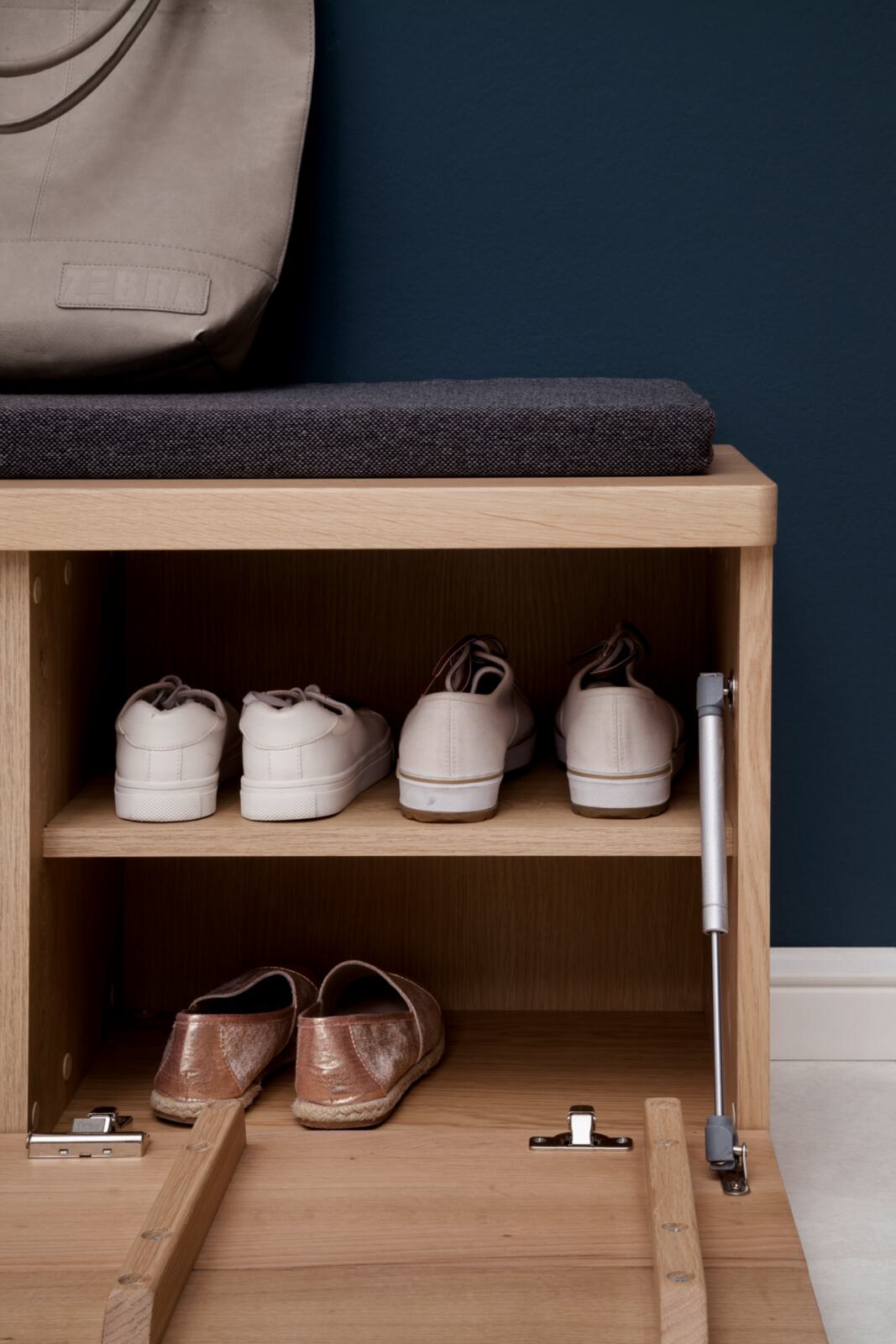 Schuhschrank aus Holz mit Schuhen und Tasche. Sitzbank mit grauem Kissen.