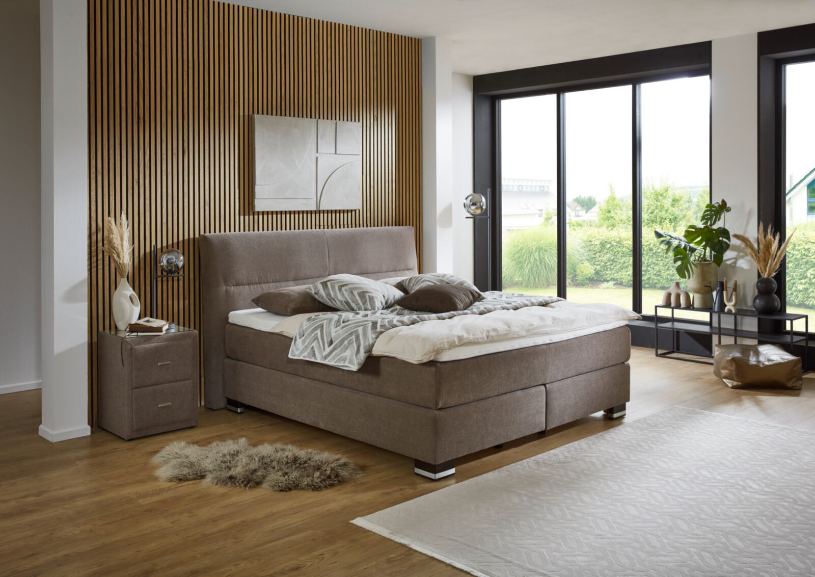 Modernes Schlafzimmer mit Boxspringbett, Holzpaneelwand und großem Fenster.