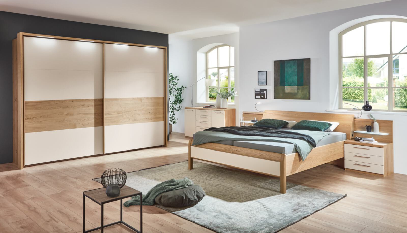 Modernes Schlafzimmer mit Holzbett, Schiebetürenschrank und viel Tageslicht.