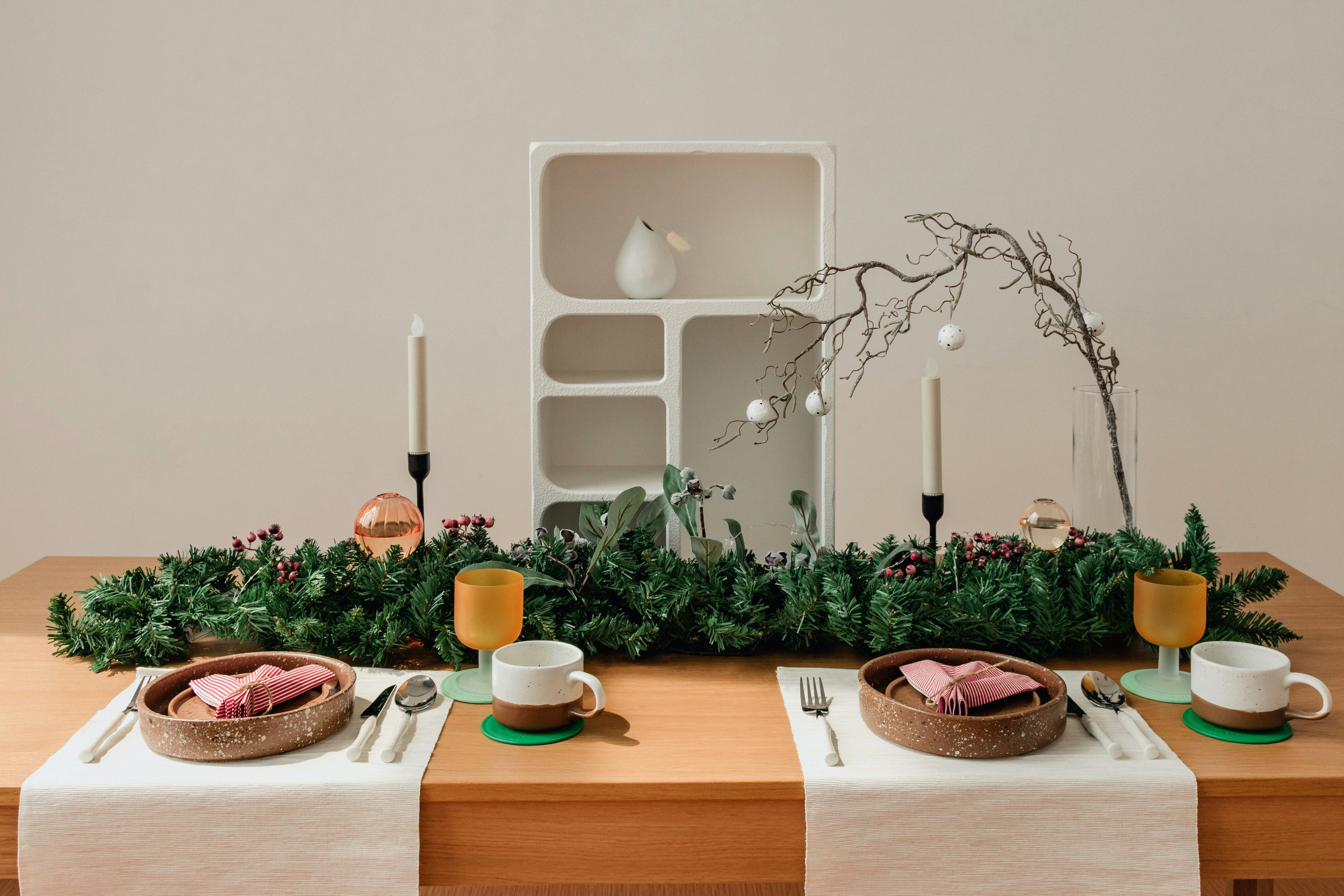 Festliche Tischdekoration mit Tannengrün, Kerzen und modernem Geschirr für stimmiges Weihnachtsambiente.