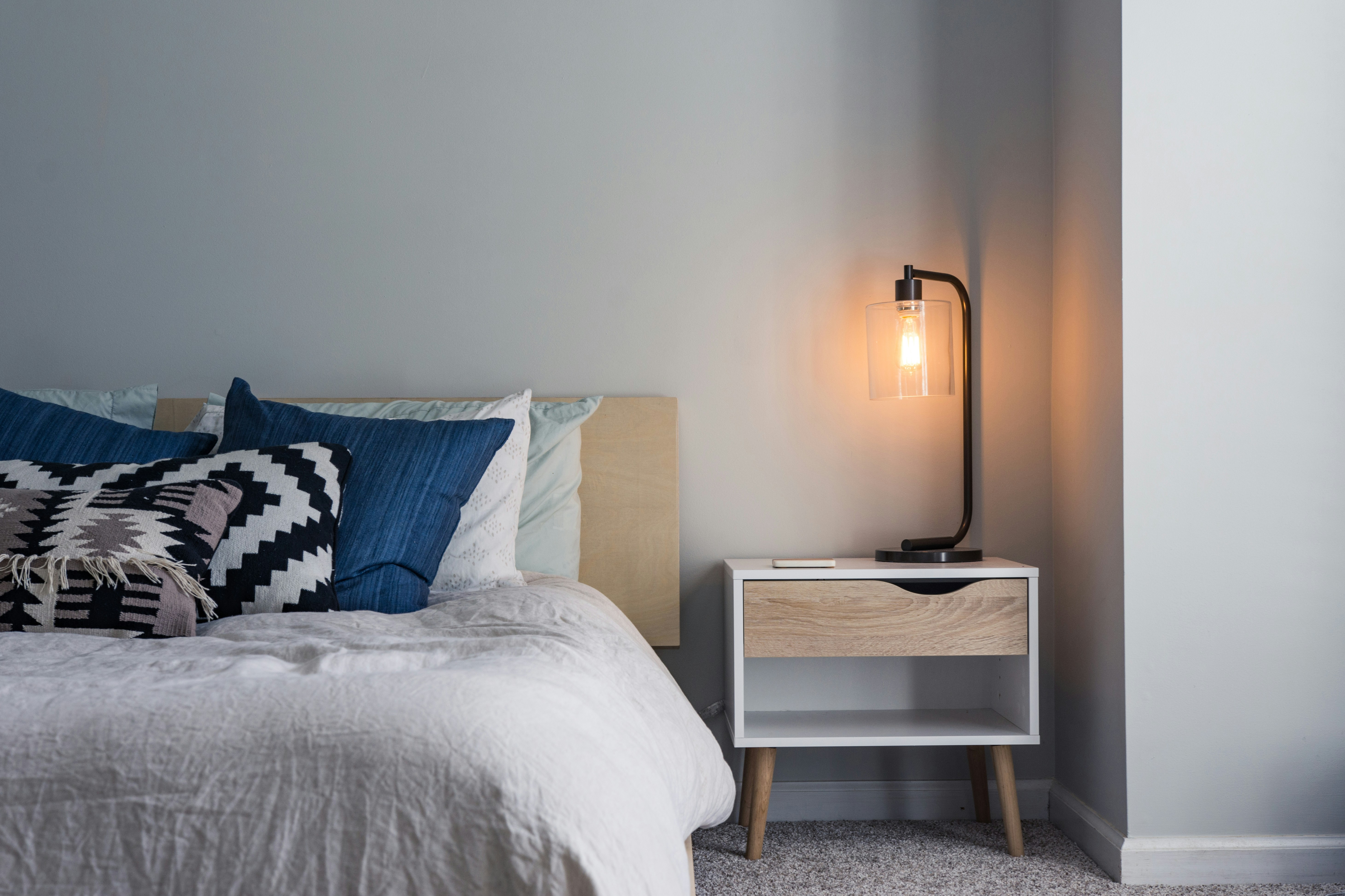Schlafzimmer-Check: Bett mit Kissen und Nachttischlampe für besseren Schlaf im Winter.