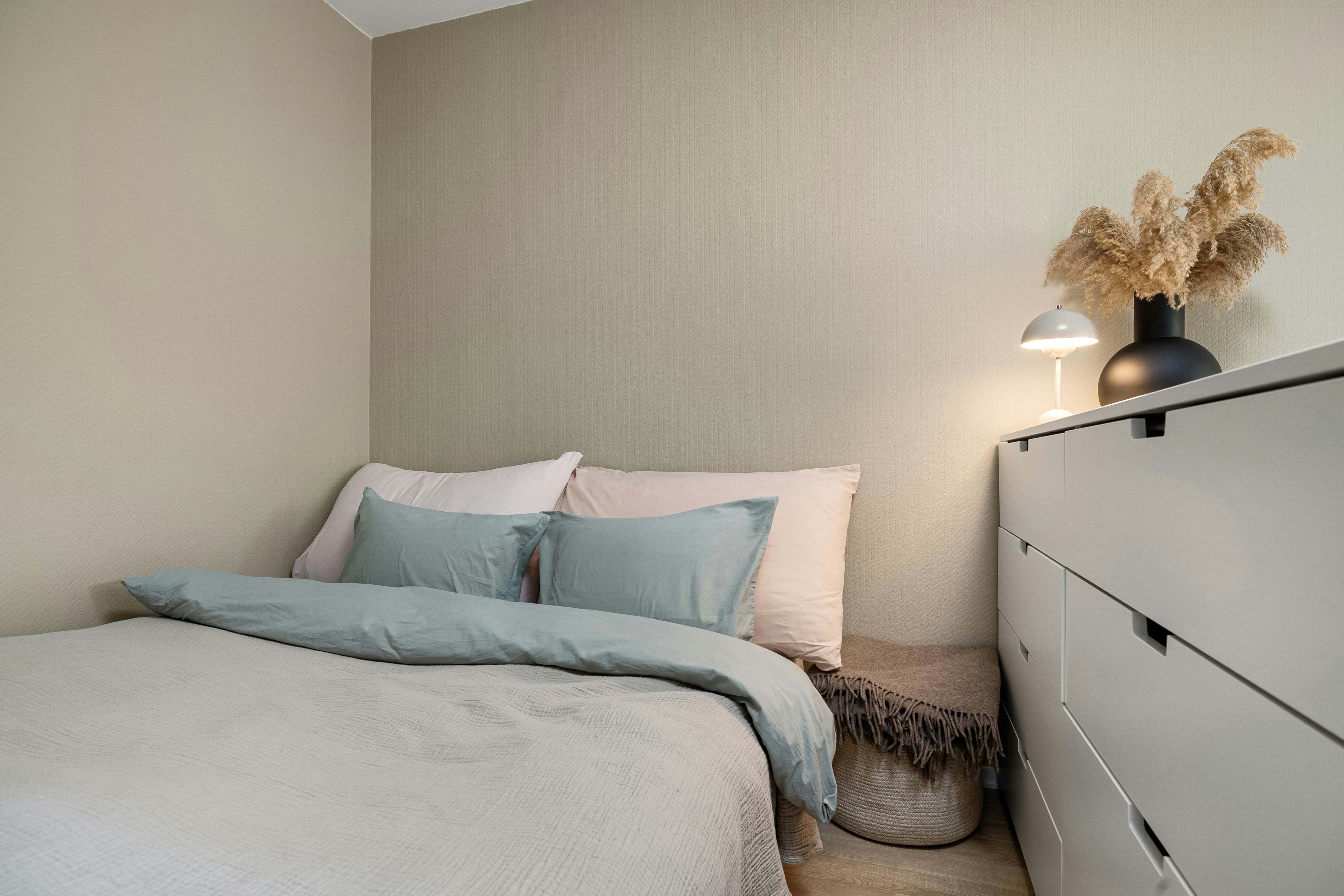 Schlafzimmer mit Bett, Kommode, Lampe und Deko. Gemütliches Ambiente für besseren Schlaf im Winter.