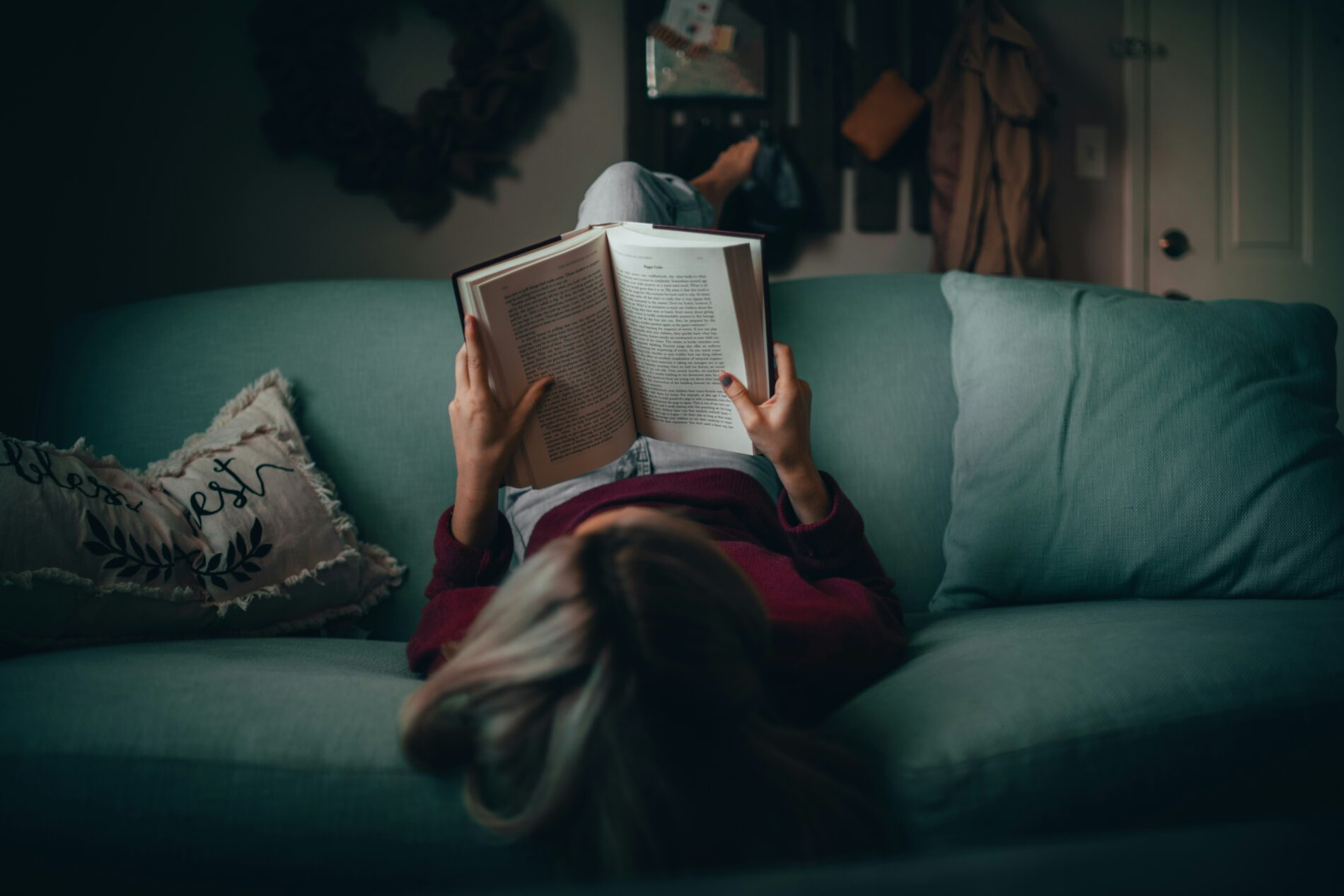 Frau liest entspannt ein Buch auf einem türkisfarbenen Sofa. Gemütliches Zuhause im Winter.